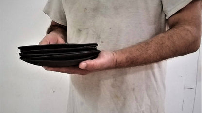 האמן קרמיקה יוסי מלכה אוחז צלחות קרמיקה שחורות